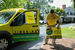 Mosquito Joe Technician Placing Mosquito Joe Sign in Yard with Van in Background